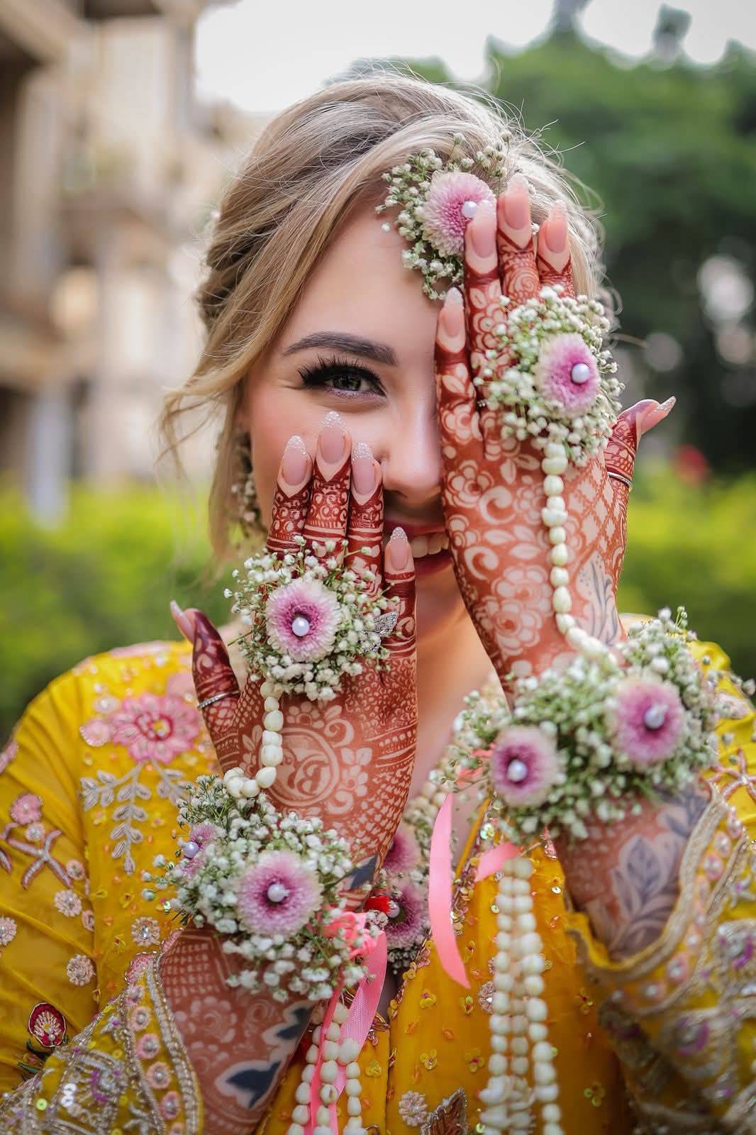 Bride wearing fresh floral jewelry and henna on her mehndi day, hair and makeup by Eleglam
