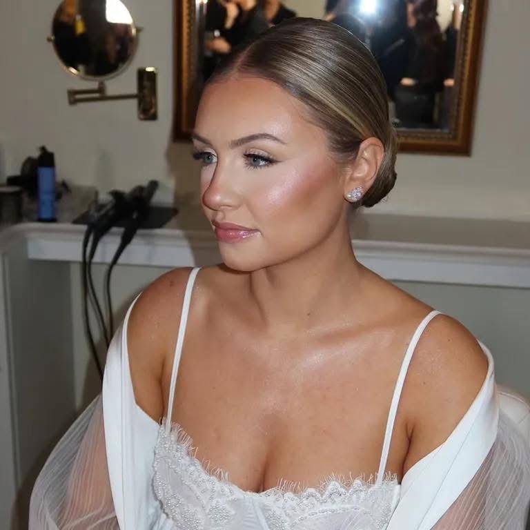 Bride in a sleek low updo with luminous skin and a soft nude lip, hair and makeup by Eleglam